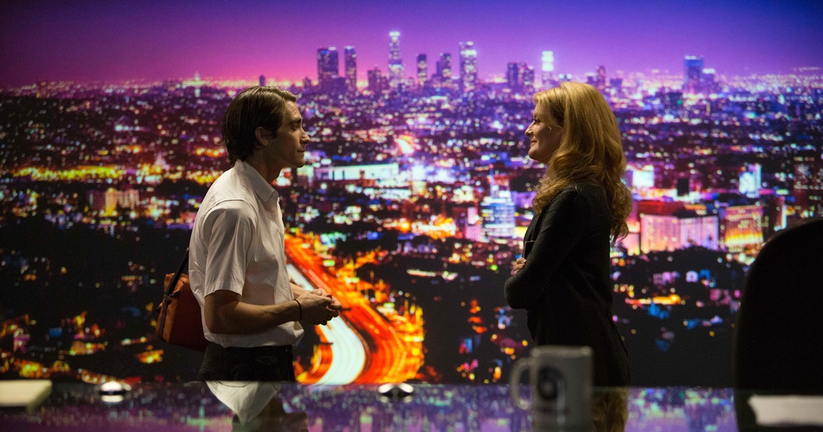 مردی با دوربین خبری در نیمه‌شب، چراغ‌های پلیس در پس‌زمینه می‌درخشند