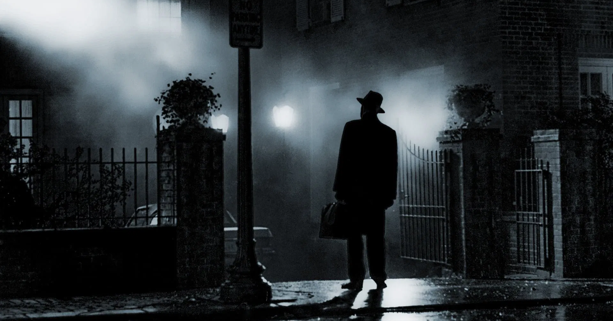 تصویری از یک کشیش با کلاه و چمدان، ایستاده در برابر خانه‌ای در شب، با نور چراغی که او را روشن کرده است
